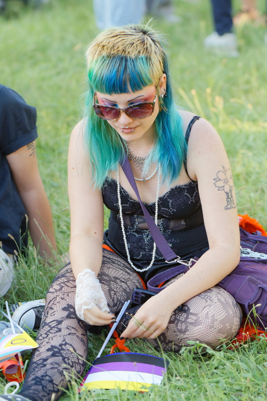 20 - Person sitting on grass wearing a black lace top with a layered necklace, sunglasses, and black patterned tights